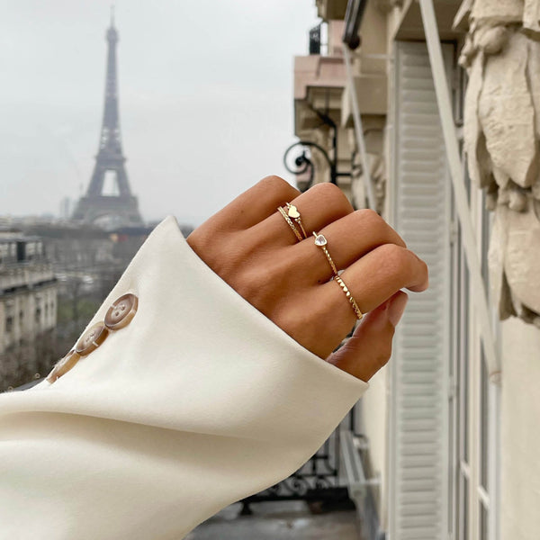 Elegant hand wearing gold rings, 24KAE JEWELS JEWELRY Mod. 12417Y/56, with Eiffel Tower in the background.