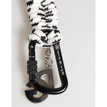 Black carabiner clip with white and black woven rope and metal attachments on a neutral background.