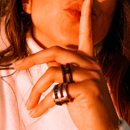 Woman wearing rings from AN JEWELS JEWELRY Mod. AR.R2NS02BK-9 collection, with a finger to her lips in a shushing gesture.