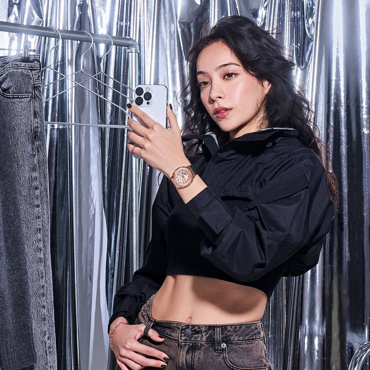 Woman wearing CASIO G-SHOCK Mod. MINI OAK G-STEEL wristwatch, posing with smartphone in metallic room.