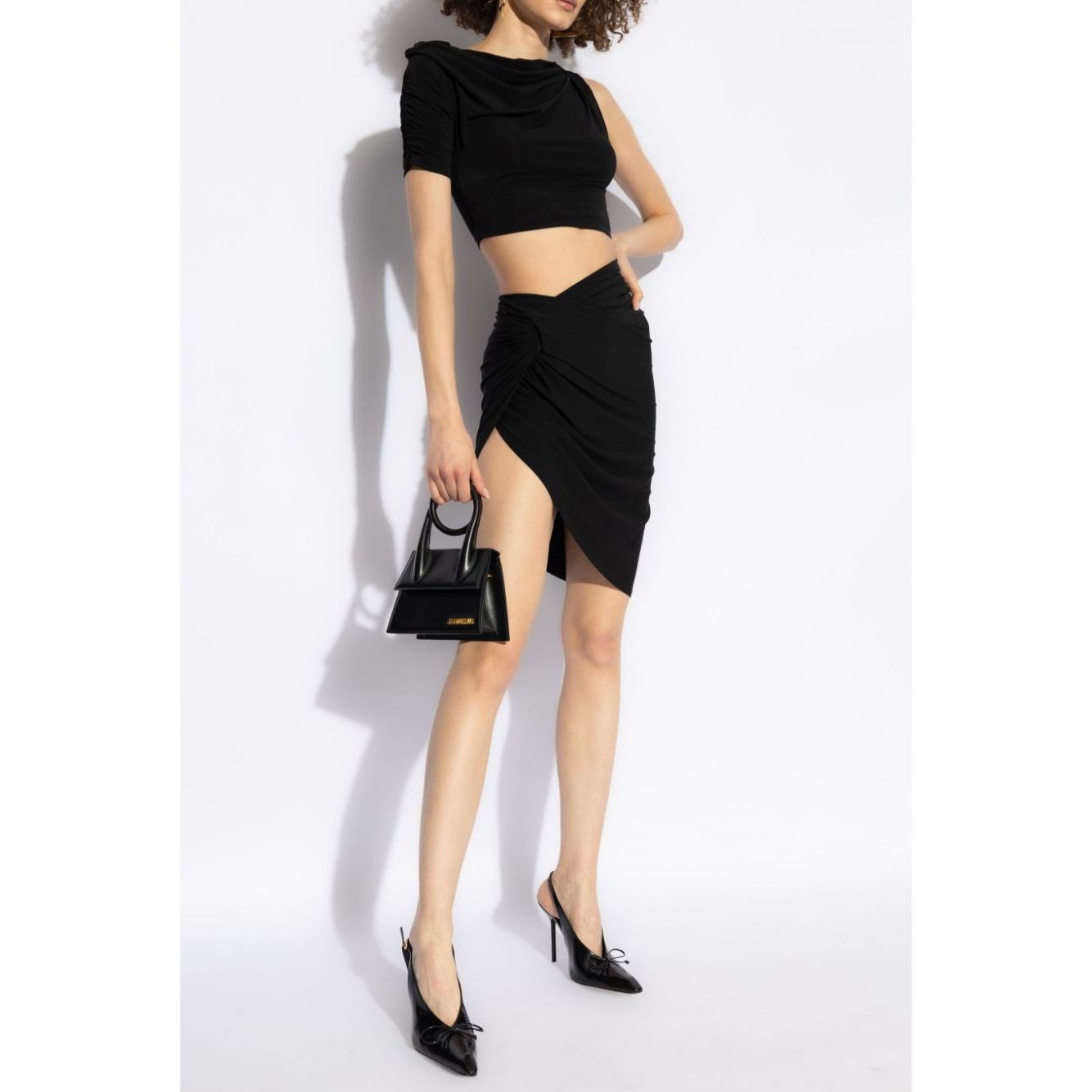 Model wearing JACQUEMUS Skirts Black, featuring a black stretch-design, draped detailing, asymmetric high-waisted thigh-length La Mini Jupe Drapeado skirt.