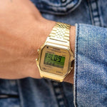 Gents wrist with TIMEX Mod. T80 gold quartz alarm wristwatch featuring digital display, worn with denim shirt, water resistant 3 ATM.