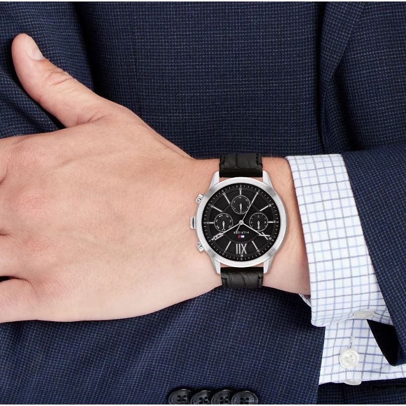Man wearing TOMMY HILFIGER Mod. 1710527 multifunction wristwatch with black dial and leather strap, quartz movement, 5 ATM water resistance.