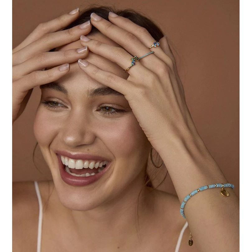 Smiling woman wearing blue stone ring and matching bracelet with hands on face.